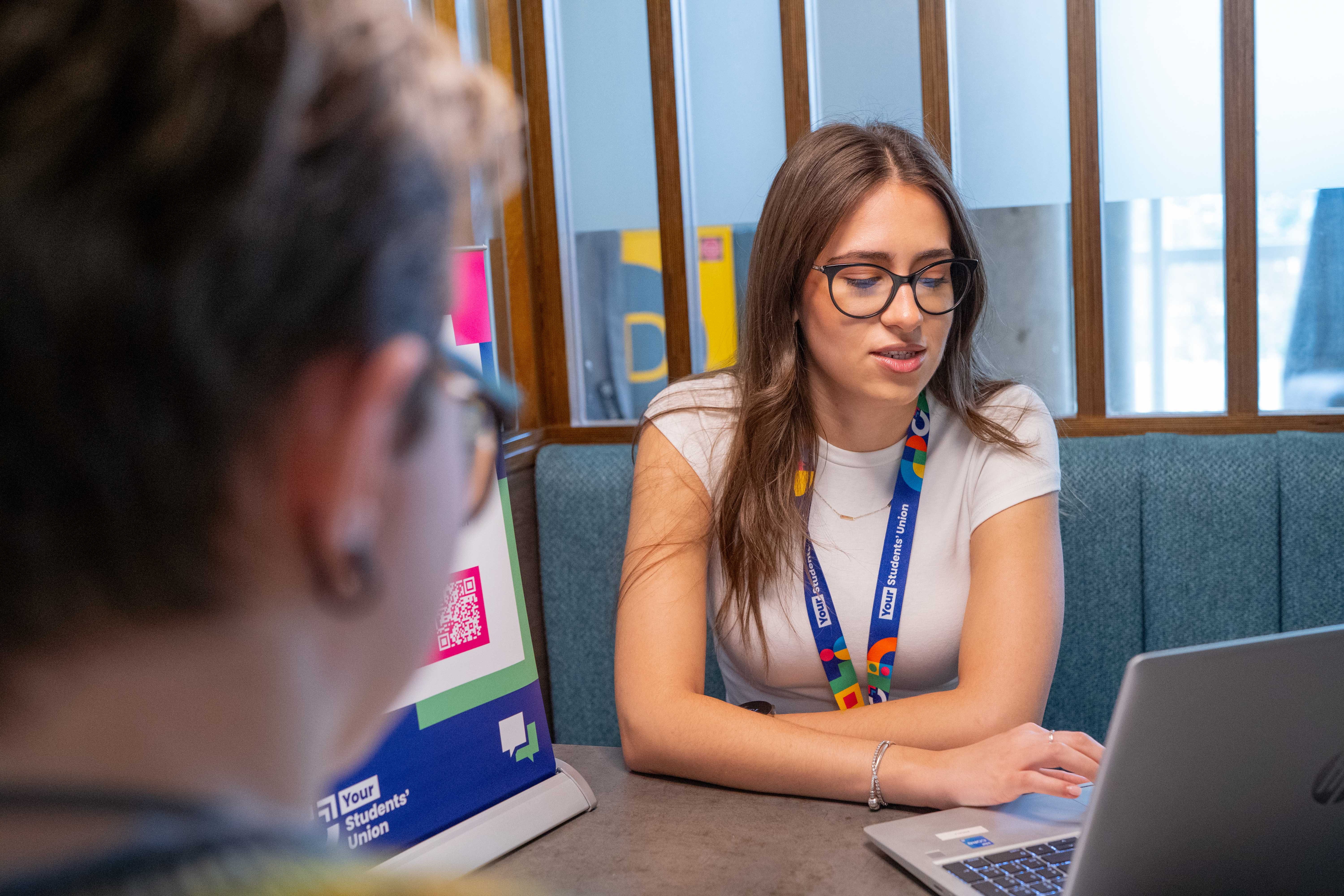 Two students sat within a private booth having a meeting. One student is looking at a laptop.