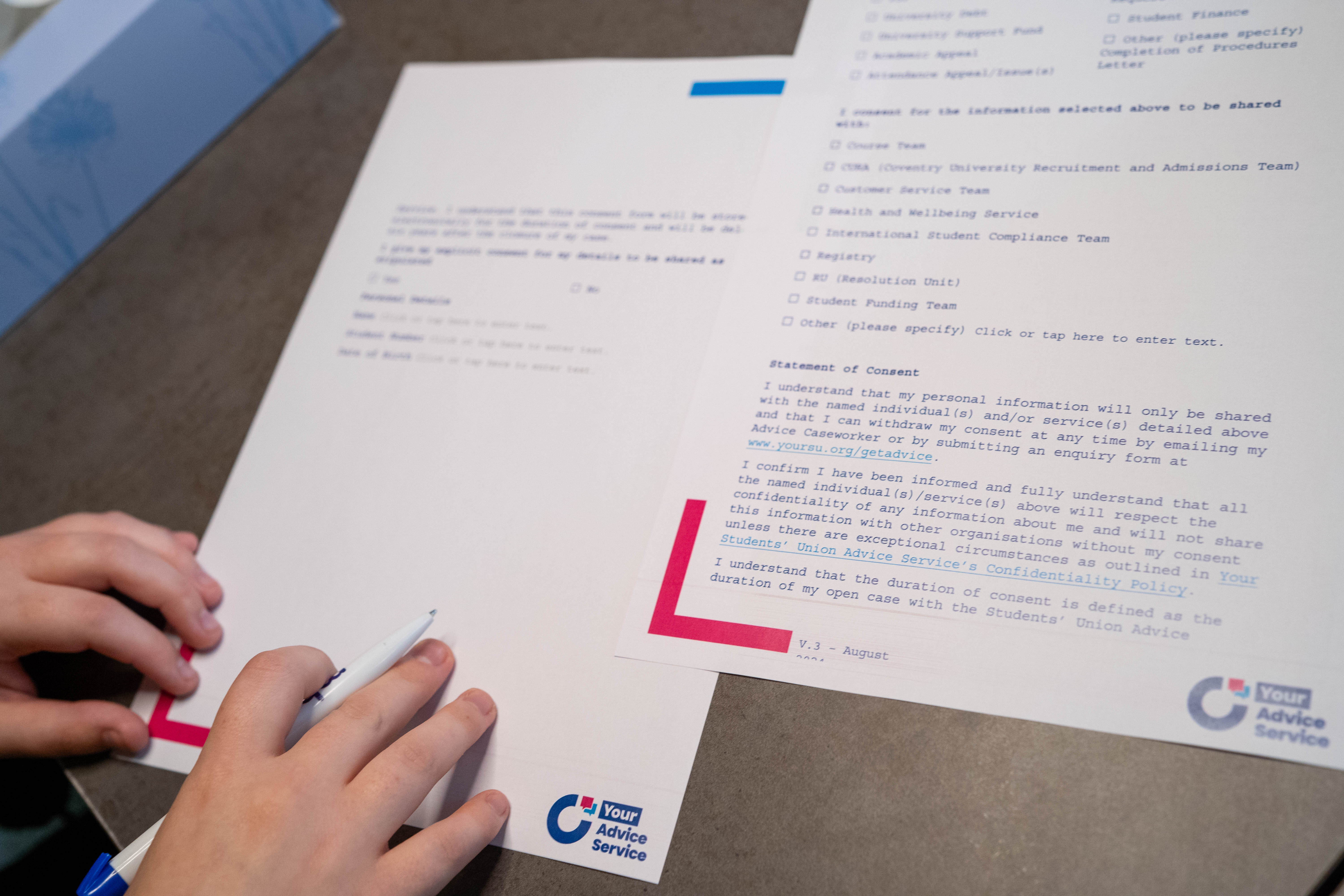 Two pieces of paper laying on a table with a pair of hands touching one of those pieces.